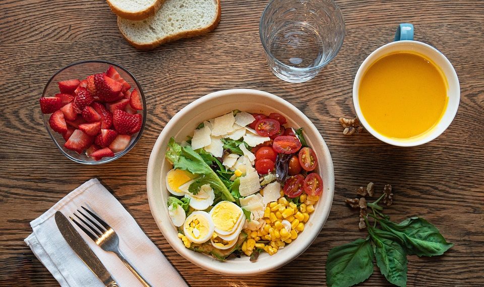 Healthy salad with eggs, corn, and tomatoes next to strawberries and orange juice.
