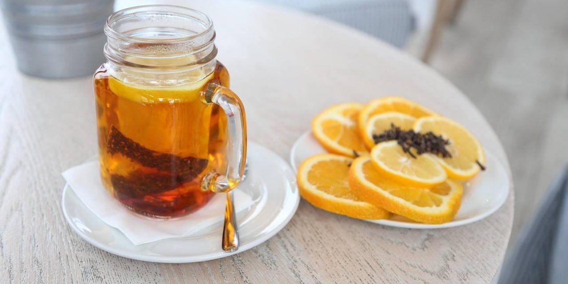 Hot tea in a glass mug with sliced oranges and cloves on a table.