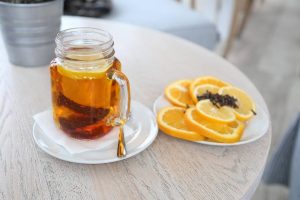 Hot tea in a glass mug with sliced oranges and cloves on a table.