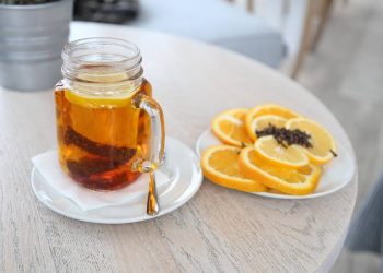 Hot tea in a glass mug with sliced oranges and cloves on a table.