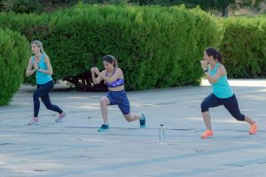 Women doing outdoor lunges in a sunny park workout.