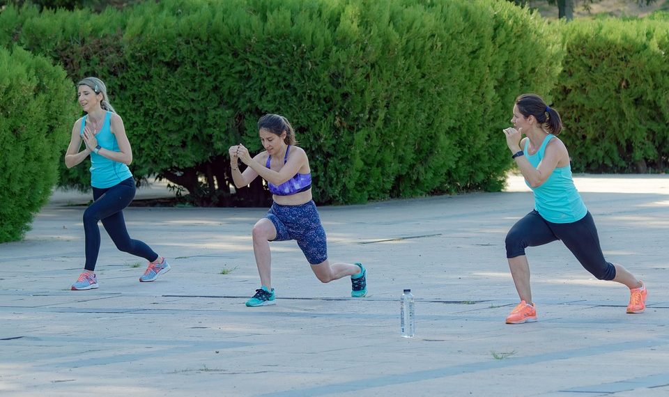 Women doing outdoor lunges in a sunny park workout.