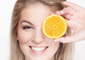Woman smiling, holding a slice of orange over her eye.