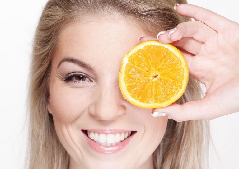 Woman smiling, holding a slice of orange over her eye.