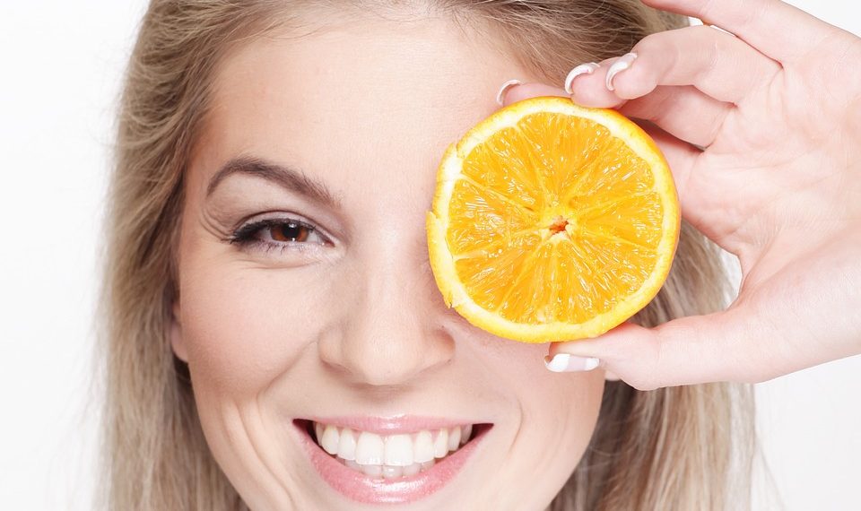 Woman smiling, holding a slice of orange over her eye.