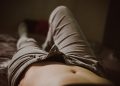 Lying on bed in unbuttoned khaki pants, relaxed and casual.