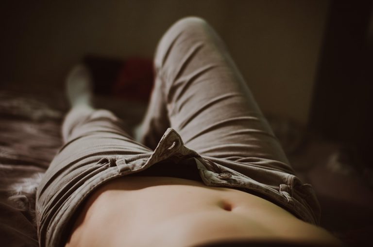 Lying on bed in unbuttoned khaki pants, relaxed and casual.
