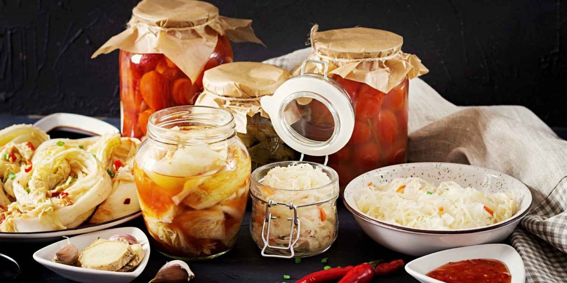 Jars of homemade pickled vegetables and sauerkraut on a kitchen table.