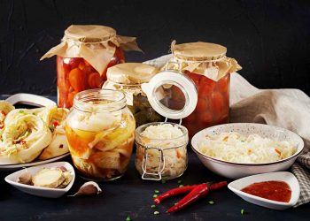 Jars of homemade pickled vegetables and sauerkraut on a kitchen table.