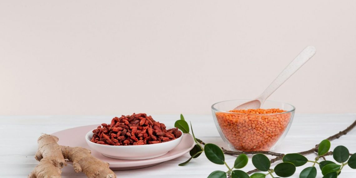 Ginger, goji berries, and lentils arranged on a white table with green leaves.