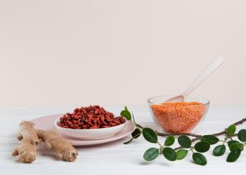 Ginger, goji berries, and lentils arranged on a white table with green leaves.
