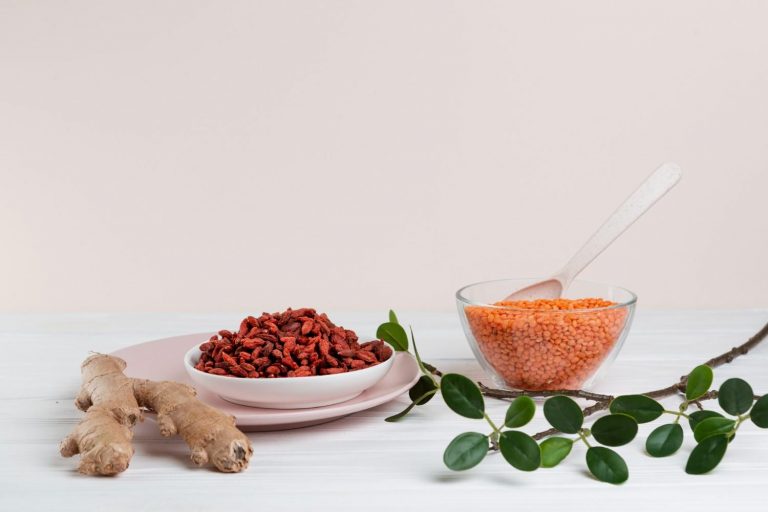 Ginger, goji berries, and lentils arranged on a white table with green leaves.