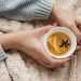 Hands holding a cup of warm tea with lemon and spice on a cozy knit blanket.