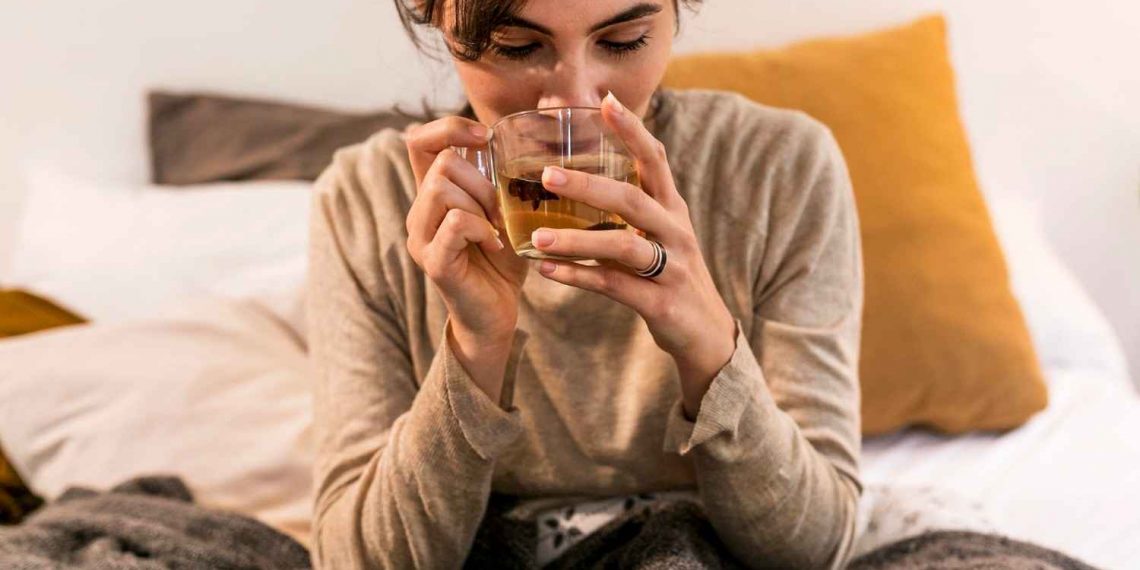 Woman enjoying a warm herbal tea in bed.
