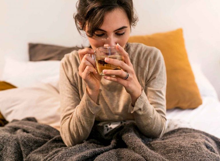 Woman enjoying a warm herbal tea in bed.