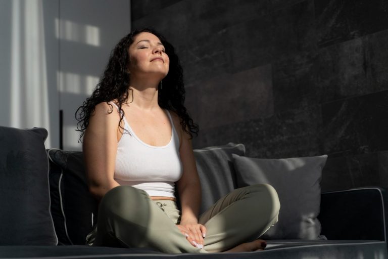 Woman meditating on couch, eyes closed, enjoying sunbeam.