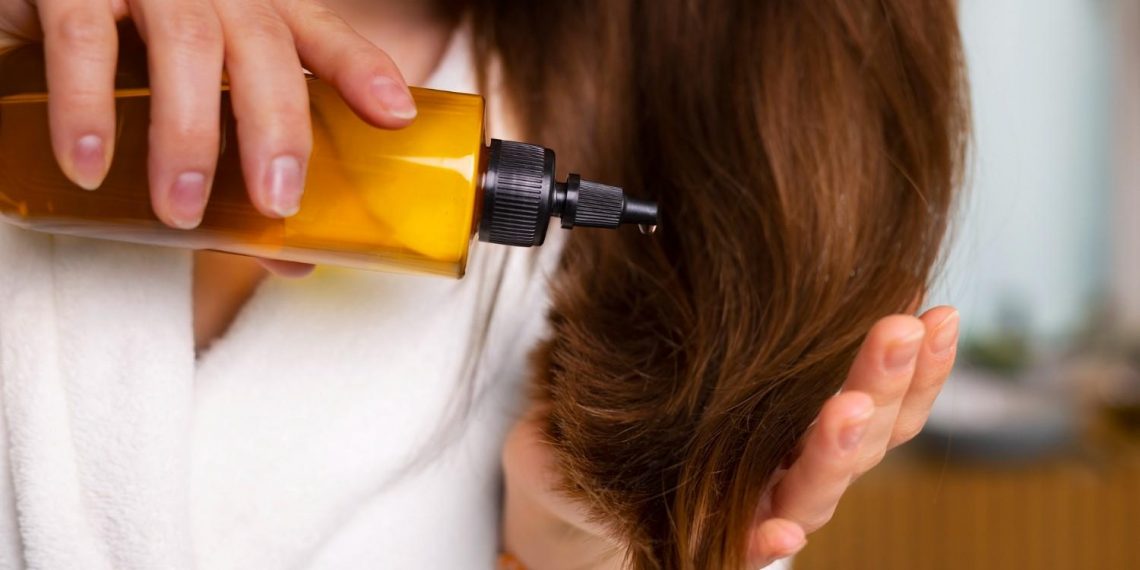 Woman applying hair oil in bathroom.