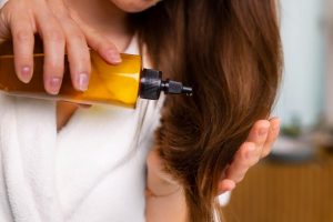 Woman applying hair oil in bathroom.