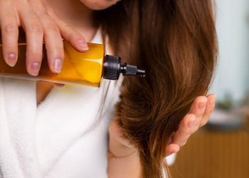 Woman applying hair oil in bathroom.