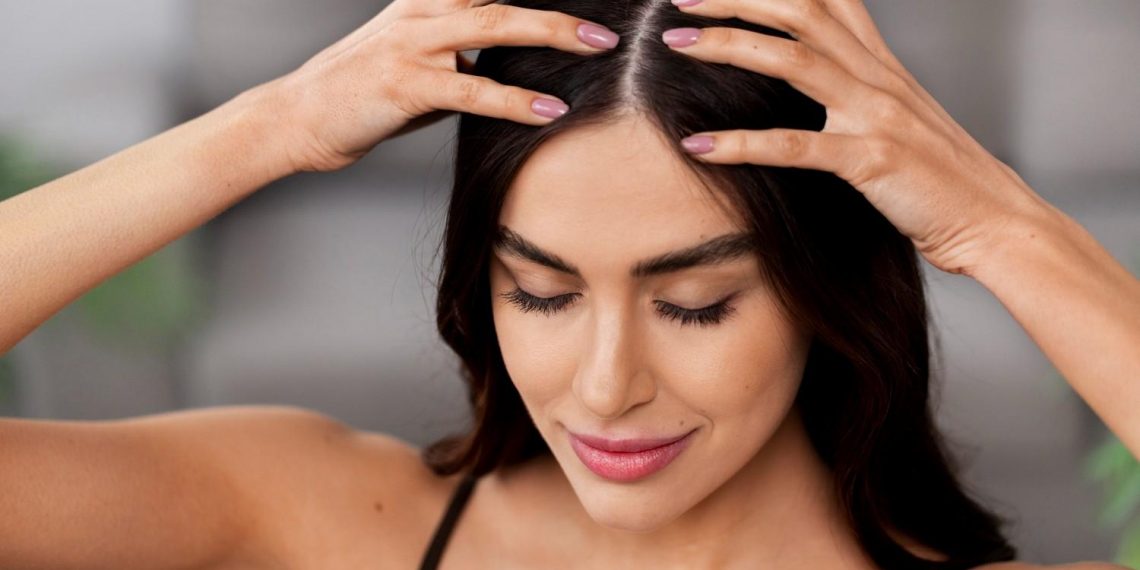 Woman performing a calming scalp massage with eyes closed.