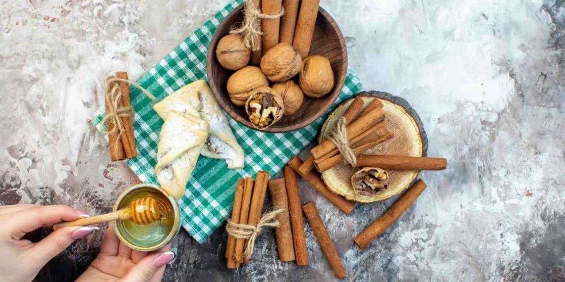 Hands pouring honey over walnuts and cinnamon on a green checkered cloth.