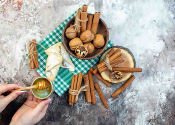 Hands pouring honey over walnuts and cinnamon on a green checkered cloth.