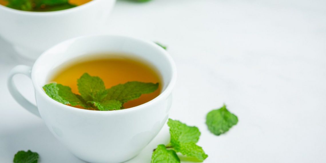 Brewed herbal mint tea in a white cup with fresh mint leaves