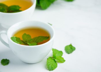Brewed herbal mint tea in a white cup with fresh mint leaves
