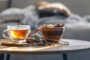 Warm cup of herbal tea with spices and strainer on table.
