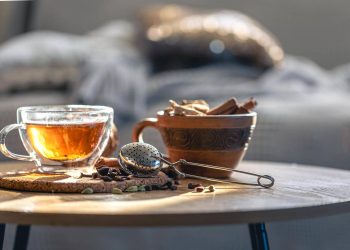Warm cup of herbal tea with spices and strainer on table.