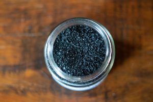 Jar filled with activated charcoal granules on wooden table.