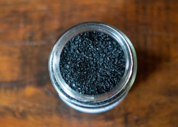 Jar filled with activated charcoal granules on wooden table.
