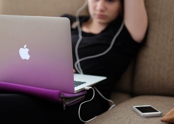 Young woman using a laptop on a couch with earbuds in.