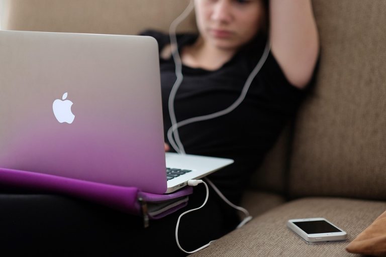 Young woman using a laptop on a couch with earbuds in.