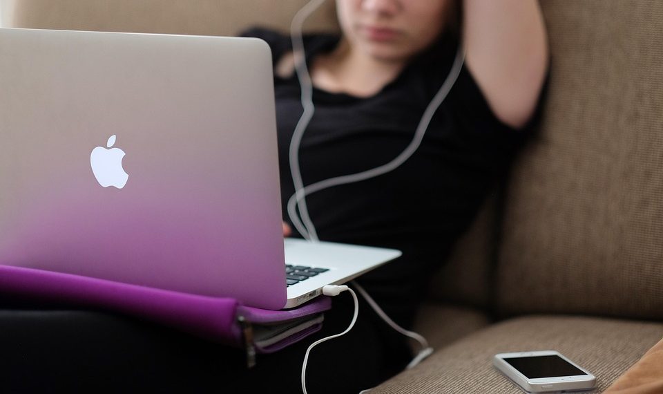 Young woman using a laptop on a couch with earbuds in.