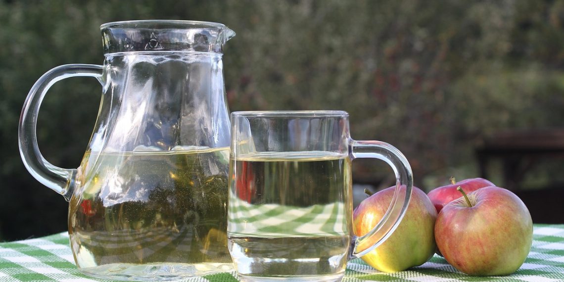 Pitcher and glass of apple juice on a checkered table.