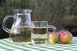 Pitcher and glass of apple juice on a checkered table.