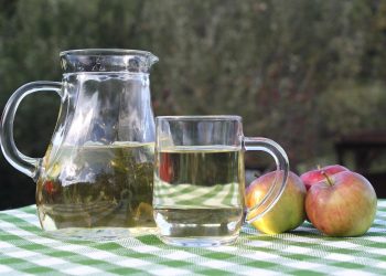 Pitcher and glass of apple juice on a checkered table.