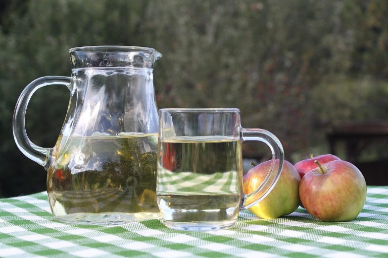Pitcher and glass of apple juice on a checkered table.