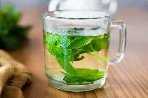 Fresh mint leaves steeping in a glass cup of herbal tea.