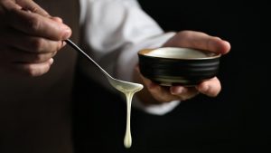 Hand drizzling creamy sauce from spoon into bowl.