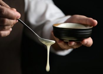 Hand drizzling creamy sauce from spoon into bowl.