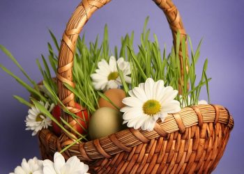 Wicker basket filled with grass, colorful eggs, and white daisies.