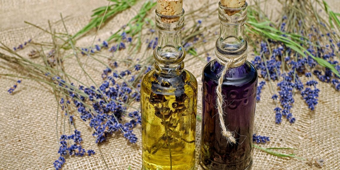Two glass bottles of essential oil surrounded by dried lavender sprigs on burlap.