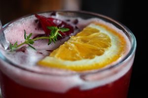 Refreshing hibiscus cocktail with orange slice garnish.