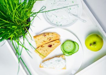 Creamy dip with toast, cucumber slices, and an apple on a tray.