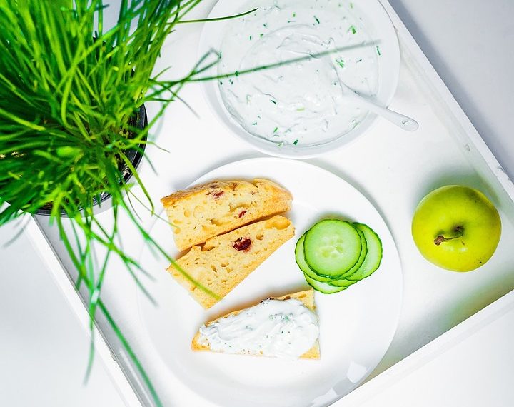 Creamy dip with toast, cucumber slices, and an apple on a tray.