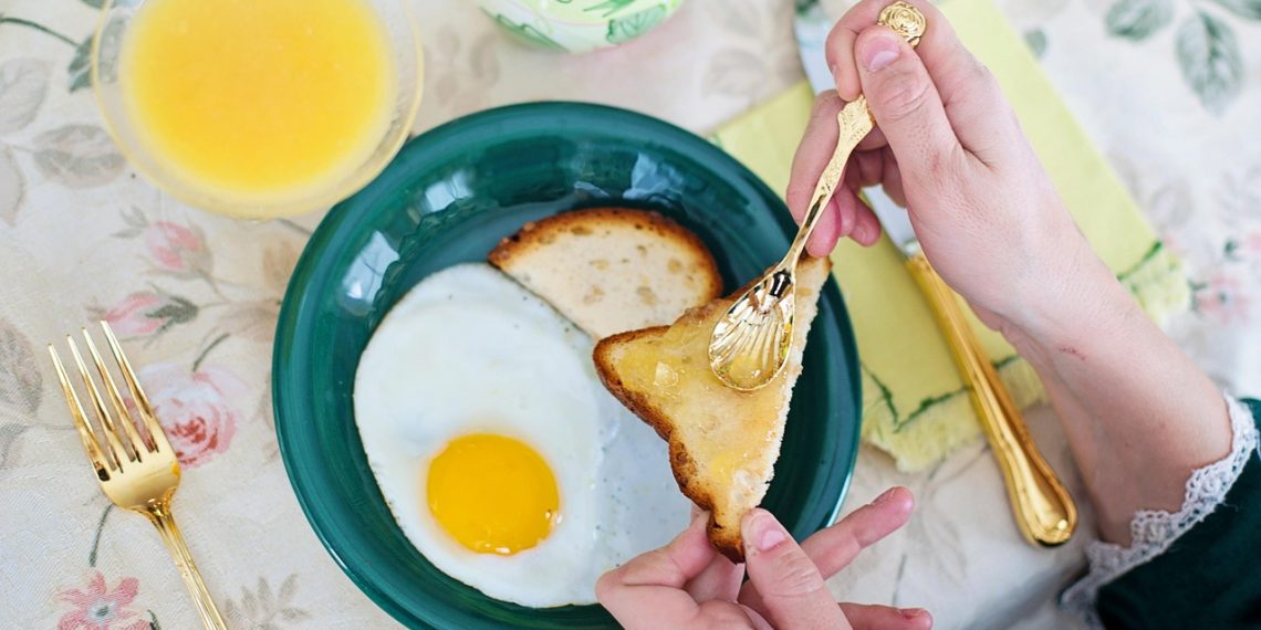 Toast with jam being spread beside fried egg and juice