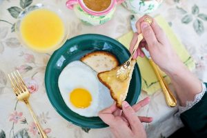 Toast with jam being spread beside fried egg and juice