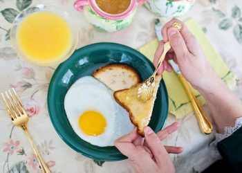 Toast with jam being spread beside fried egg and juice